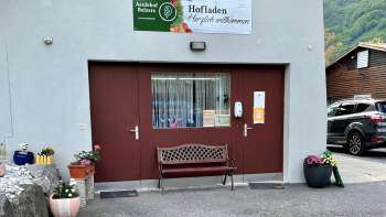 Eingang zum Hofladen Aeulehof mit rotem Tor, Sitzbank und Blumendekoration in Triesen, Liechtenstein.