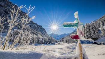 Verschneiter Wegweiser im Langlaufgebiet Valüna – Steg mit strahlender Wintersonne