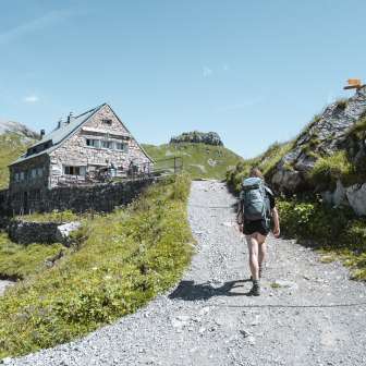Frau mit Rucksack auf einem Bergpfad kurz vor der Pfälzerhütte – alpine Kulisse, markierte Wanderroute und grüne Hochgebirgswiesen