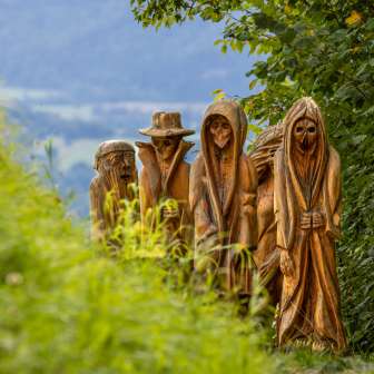 Detailansicht geschnitzter Holzfiguren in mystischer Darstellung am Walser Sagenweg in Triesenberg, umgeben von grüner Natur