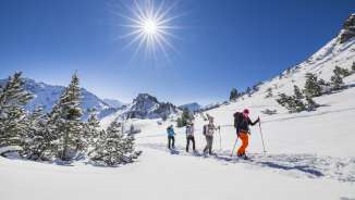 Gruppe beim Schneeschuhwandern durch die verschneite Landschaft am Schönberg bei Malbun unter strahlender Wintersonne.