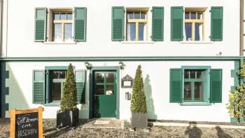 Außenansicht des Gasthauses mit großer Terrasse, umgeben von gepflegten Büschen und Bäumen