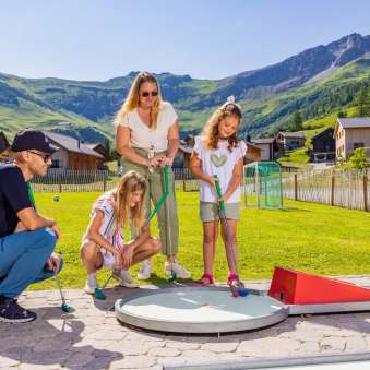 Familie spielt gemeinsam Minigolf im sonnigen Bergdorf Malbun in Liechtenstein – Spaß für Groß und Klein in den Alpen.
