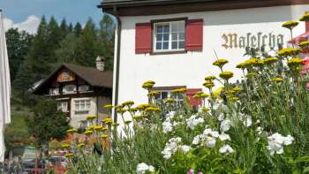 Traditionelles Berggasthaus mit rotem Fensterladen und blühenden Blumen im Vordergrund