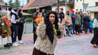 Verkleidete Schaaner Hexe beim Fasnachtsumzug in Schaan, Liechtenstein, vor Publikum und buntem Konfetti auf der Straße