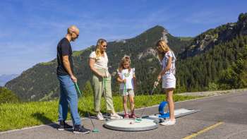  Familie spielt gemeinsam Minigolf in den Bergen von Malbun bei strahlendem Sonnenschein