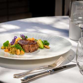 Exquisit angerichteter Fleischgang mit Gemüse und Blüten im Park Hotel Sonnenhof auf der Terrasse in Vaduz, Liechtenstein