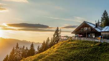 Gadafurahütte auf sonnenbeschienener Bergwiese mit Blick auf die Berge und Sonnenuntergang