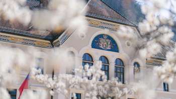 Regierungsgebäude von Vaduz eingerahmt von blühenden Bäumen im Frühling, mit Fokus auf das Landeswappen.