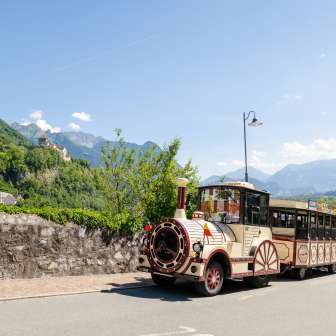 Citytrain fährt durch Vaduz, im Hintergrund Schloss Vaduz und die Alpen bei strahlendem Sonnenschein