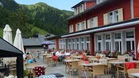 Sonnige Terrasse des Restaurants mit gedeckten Tischen, Sonnenschirmen und Alpenblick.