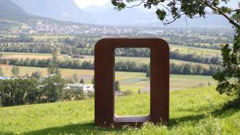 Skulptur „Resonare“ aus rostigem Metall auf der Anhöhe Krest mit Blick auf das Rheintal und die Berge im Hintergrund