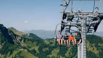 Eine Familie fährt mit der Sesselbahn Sareis über eine grüne Berglandschaft