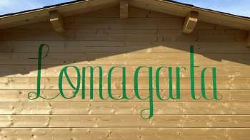 Ansicht auf das grüne Lömagarta-Logo, das stilvoll auf der Holzfassade des gemütlichen Biergartens prangt.