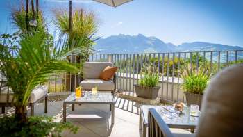Sonnige Terrasse mit modernen Loungemöbeln und Alpenpanorama im Hintergrund