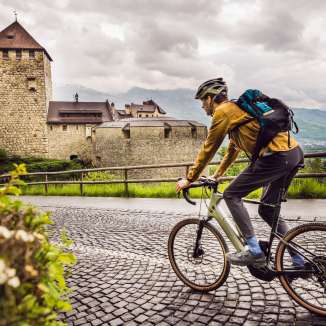 Gravelbiker fährt auf Kopfsteinpflaster Richtung Schloss Vaduz – historische Kulisse und sportlicher Ausflug in Liechtenstein