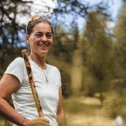 Wanderleiterin in Liechtenstein bei einer geführten Tour durch die Natur Freundliche Wanderleiterin mit Wanderstock bei einer Naturwanderung in Liechtenstein, umgeben von Bäumen und sommerlicher Landschaft.