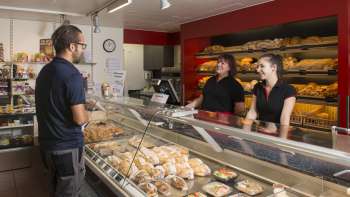 Verkaufsraum einer Bäckerei mit freundlichem Personal, frisch gebackenem Brot und Kuchen im Vordergrund