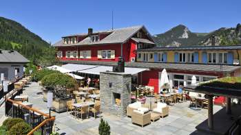 Außenansicht des Restaurants bei Sonnenschein, mit roter Fassade und bergigem Panorama.