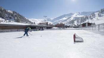 Weitläufige Eisbahn in Malbun vor beeindruckender Bergkulisse bei strahlendem Sonnenschein.