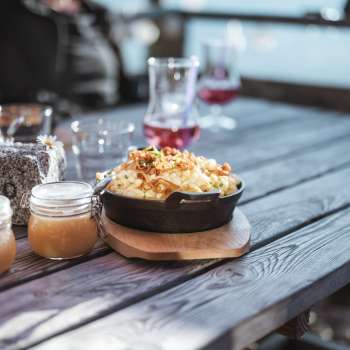 Käsknöpfle auf dem Tisch: Regionale Spezialität Käsknöpfle mit Apfelmus auf einem Holztisch vor alpiner Kulisse.