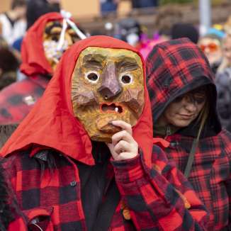Teilnehmende mit geschnitzten Holzmasken und rot-schwarzen Kostümen beim Fasnachtsumzug in Malbun