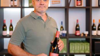 Harry Zech präsentiert eine Flasche seines Weins im stilvollen Verkaufsraum – regionale Weinkultur aus Liechtenstein.