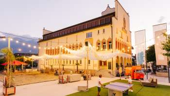 Rathausplatz Vaduz bei Abendstimmung während eines belebten Markttags mit Menschenmengen, Verkaufsständen und stimmungsvoller Beleuchtung.