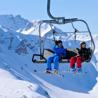 Kinder im Sessellift im Skigebiet Malbun Zwei Kinder mit Skiausrüstung fahren im Sessellift durch die verschneiten Berge von Malbun