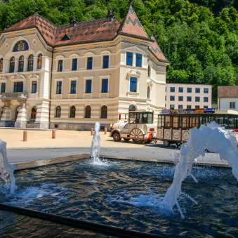 Regierungsgebäude Vaduz mit Citytrain und Brunnen Blick auf das Regierungsgebäude in Vaduz mit vorbeifahrendem Citytrain und Wasserfontänen im Vordergrund