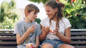 Zwei Kinder, die ein Eis auf einer Holzbank vor der Eisdiele geniessen