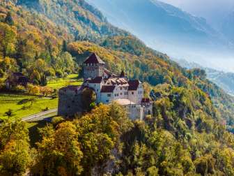 Schloss Vaduz auf einem bewaldeten Hügel in herbstlicher Landschaft in Liechtenstein