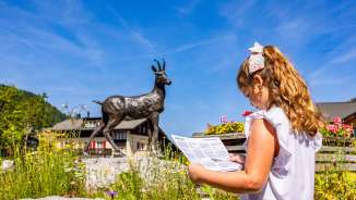 Mädchen mit Karte vor der Gemsenstatue in Malbun – kindgerechte Erkundungstour im Familienferienort in Liechtenstein.