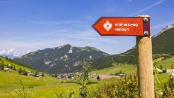 Wegweiser Alpherzweg mit Bergdorf Malbun im Hintergrund