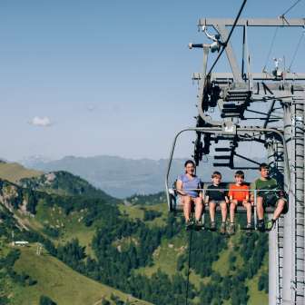 Familie mit Kindern auf einem Sessellift über den grünen Bergen von Malbun – Sommererlebnis und Panoramablick in Liechtenstein
