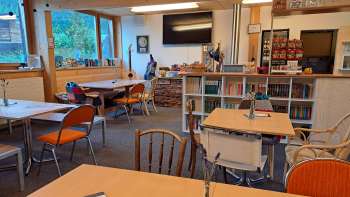 Blick auf den Gastraum mit Holzwand und Wanddeko – Mehrere Tische mit Bestuhlung und Blick auf die dekorative Wand mit Gitarren und grünen Bildern.