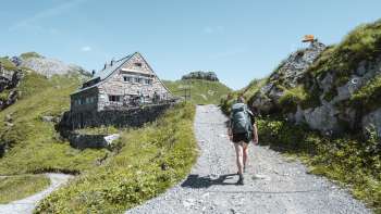 Wanderin mit Rucksack geht auf einem Bergpfad auf die Pfälzerhütte in den Liechtensteiner Alpen zu.