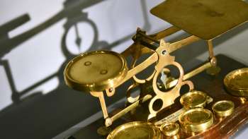Bild einer antiken goldfarbenen Balkenwaage mit verschiedenen Gewichten, ausgestellt im PostMuseum in Vaduz