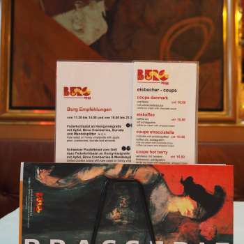 Brasserie Burg Speisekarte vor farbigem Wandbild – Kulinarik und Kunst im Herzen von Vaduz.