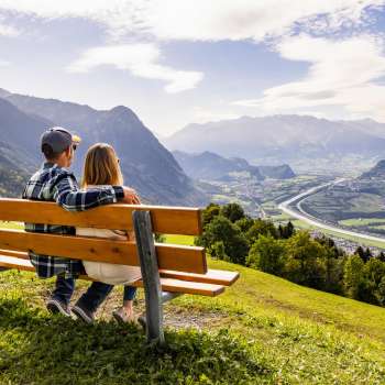Paar auf einer Holzbank mit Aussicht auf das Rheintal und die Berge.