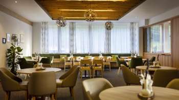 Ein weiterer Winkel des Essbereichs, mit den gleichen runden Tischen, einer gemütlichen Atmosphäre und modernen Lichtinstallationen.