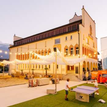 Rathausplatz Vaduz bei Abendstimmung während eines belebten Markttags mit Menschenmengen, Verkaufsständen und stimmungsvoller Beleuchtung.
