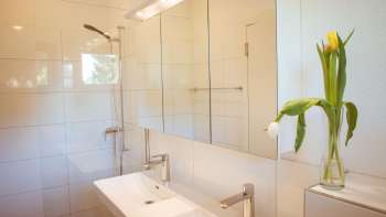 Modernes, hell gefliestes Badezimmer im Gästehaus beim Camping Mittagsspitze mit Doppelwaschbecken, Spiegel und frischen Blumen.