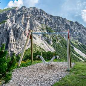 Hängeschaukel auf dem Schaukelpfad Malbun mit Blick auf steile Felswände und alpine Landschaft in Liechtenstein