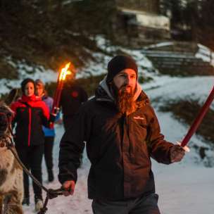 Gruppe bei einer geführten Lamawanderung im verschneiten Liechtenstein mit Fackeln – stimmungsvolles Outdoor-Abenteuer für Groß und Klein.