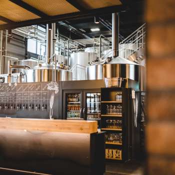Innenansicht einer Brauerei mit Brauanlage aus Edelstahl und einladendem Schanktresen im Vordergrund.