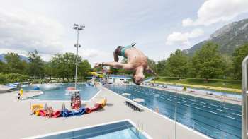 unge springt mit Salto vom 1-Meter-Brett ins Becken des Schwimmbads Mühleholz – Sommerfreude pur.