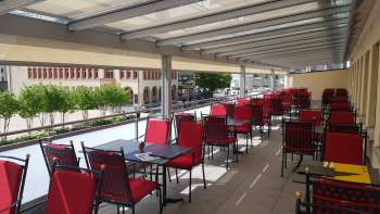 Sonnige Terrasse mit roten Stühlen und weiss gedeckten Tischen