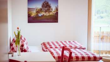 Gemütliches Doppelzimmer im Gästehaus beim Camping Mittagsspitze mit rot-weiß karierter Bettwäsche und Dekoration.