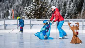 Familie auf dem Eisplatz beim Schlucher-Treff in Malbun, unterstützt von einer Eislaufhilfe in Form eines blauen Tieres